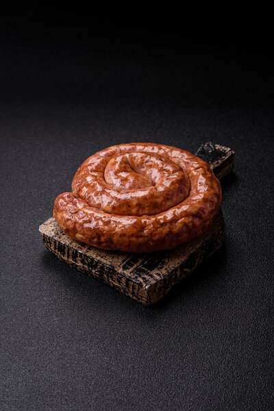 Вкусная домашняя колбаса в форме улитки или спирали, с солью и специями на темном бетонном фоне