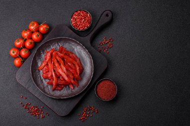 Kurutulmuş tavuk dilimleri, kurutulmuş et, kiraz ya da erik aromalı, tuzlu ve baharatlı koyu beton arka planda.