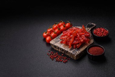 Kurutulmuş tavuk dilimleri, kurutulmuş et, kiraz ya da erik aromalı, tuzlu ve baharatlı koyu beton arka planda.