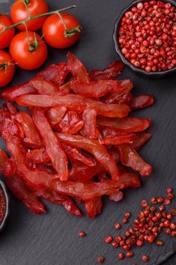 Kurutulmuş tavuk dilimleri, kurutulmuş et, kiraz ya da erik aromalı, tuzlu ve baharatlı koyu beton arka planda.