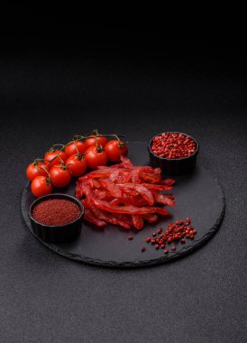 Kurutulmuş tavuk dilimleri, kurutulmuş et, kiraz ya da erik aromalı, tuzlu ve baharatlı koyu beton arka planda.