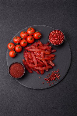 Kurutulmuş tavuk dilimleri, kurutulmuş et, kiraz ya da erik aromalı, tuzlu ve baharatlı koyu beton arka planda.