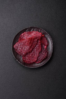 Kurutulmuş sığır eti dilimleri, kurutulmuş et, kiraz veya erik aromalı, tuz ve baharatlar koyu beton arka planda.