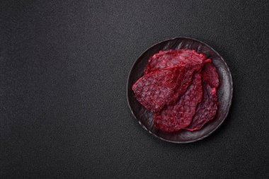 Kurutulmuş sığır eti dilimleri, kurutulmuş et, kiraz veya erik aromalı, tuz ve baharatlar koyu beton arka planda.