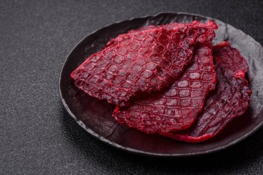 Kurutulmuş sığır eti dilimleri, kurutulmuş et, kiraz veya erik aromalı, tuz ve baharatlar koyu beton arka planda.