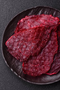 Kurutulmuş sığır eti dilimleri, kurutulmuş et, kiraz veya erik aromalı, tuz ve baharatlar koyu beton arka planda.