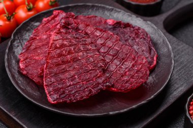 Kurutulmuş sığır eti dilimleri, kurutulmuş et, kiraz veya erik aromalı, tuz ve baharatlar koyu beton arka planda.