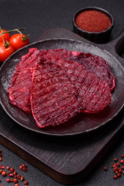 Kurutulmuş sığır eti dilimleri, kurutulmuş et, kiraz veya erik aromalı, tuz ve baharatlar koyu beton arka planda.