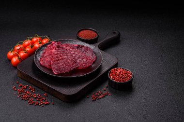 Kurutulmuş sığır eti dilimleri, kurutulmuş et, kiraz veya erik aromalı, tuz ve baharatlar koyu beton arka planda.