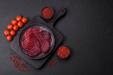 Kurutulmuş sığır eti dilimleri, kurutulmuş et, kiraz veya erik aromalı, tuz ve baharatlar koyu beton arka planda.