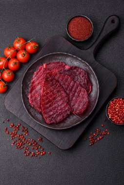 Kurutulmuş sığır eti dilimleri, kurutulmuş et, kiraz veya erik aromalı, tuz ve baharatlar koyu beton arka planda.