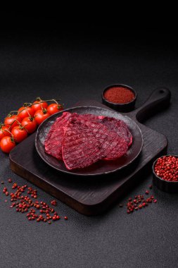 Kurutulmuş sığır eti dilimleri, kurutulmuş et, kiraz veya erik aromalı, tuz ve baharatlar koyu beton arka planda.