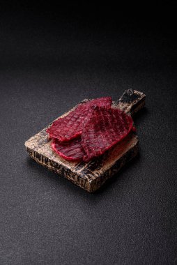 Kurutulmuş sığır eti dilimleri, kurutulmuş et, kiraz veya erik aromalı, tuz ve baharatlar koyu beton arka planda.