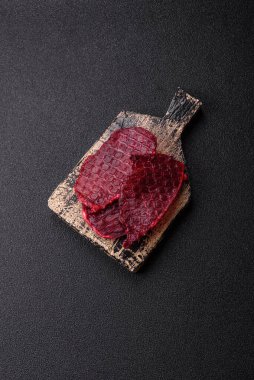 Kurutulmuş sığır eti dilimleri, kurutulmuş et, kiraz veya erik aromalı, tuz ve baharatlar koyu beton arka planda.