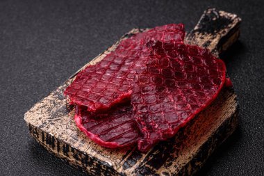 Kurutulmuş sığır eti dilimleri, kurutulmuş et, kiraz veya erik aromalı, tuz ve baharatlar koyu beton arka planda.