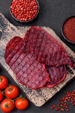 Kurutulmuş sığır eti dilimleri, kurutulmuş et, kiraz veya erik aromalı, tuz ve baharatlar koyu beton arka planda.