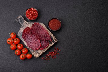 Kurutulmuş sığır eti dilimleri, kurutulmuş et, kiraz veya erik aromalı, tuz ve baharatlar koyu beton arka planda.