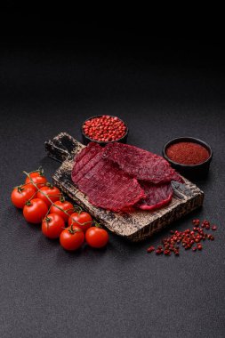 Kurutulmuş sığır eti dilimleri, kurutulmuş et, kiraz veya erik aromalı, tuz ve baharatlar koyu beton arka planda.