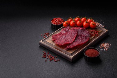 Kurutulmuş sığır eti dilimleri, kurutulmuş et, kiraz veya erik aromalı, tuz ve baharatlar koyu beton arka planda.