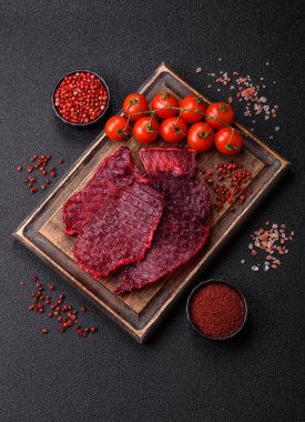 Kurutulmuş sığır eti dilimleri, kurutulmuş et, kiraz veya erik aromalı, tuz ve baharatlar koyu beton arka planda.