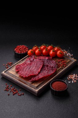 Kurutulmuş sığır eti dilimleri, kurutulmuş et, kiraz veya erik aromalı, tuz ve baharatlar koyu beton arka planda.