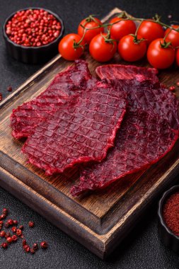 Kurutulmuş sığır eti dilimleri, kurutulmuş et, kiraz veya erik aromalı, tuz ve baharatlar koyu beton arka planda.