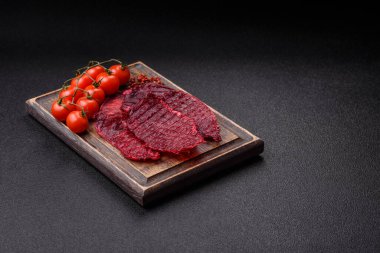 Kurutulmuş sığır eti dilimleri, kurutulmuş et, kiraz veya erik aromalı, tuz ve baharatlar koyu beton arka planda.