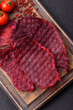 Kurutulmuş sığır eti dilimleri, kurutulmuş et, kiraz veya erik aromalı, tuz ve baharatlar koyu beton arka planda.