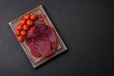 Kurutulmuş sığır eti dilimleri, kurutulmuş et, kiraz veya erik aromalı, tuz ve baharatlar koyu beton arka planda.