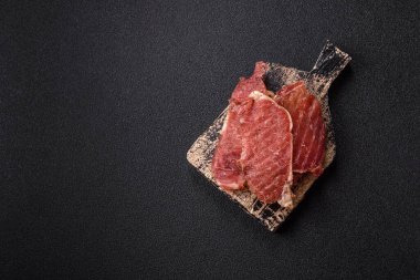 Kurutulmuş et, tuz ve baharatla birlikte koyu beton arka planda dilimler.