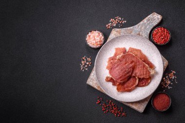 Kurutulmuş et, tuz ve baharatla birlikte koyu beton arka planda dilimler.