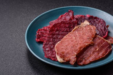 Kurutulmuş et, tuz ve baharatla birlikte koyu beton arka planda dilimler.