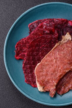 Kurutulmuş et, tuz ve baharatla birlikte koyu beton arka planda dilimler.