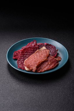 Kurutulmuş et, tuz ve baharatla birlikte koyu beton arka planda dilimler.