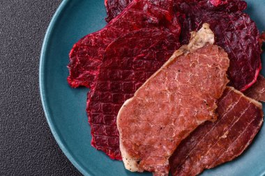 Kurutulmuş et, tuz ve baharatla birlikte koyu beton arka planda dilimler.