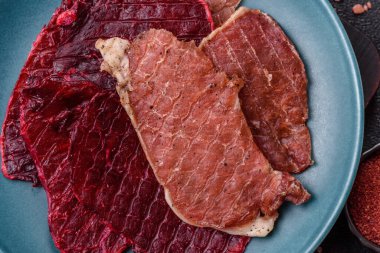 Kurutulmuş et, tuz ve baharatla birlikte koyu beton arka planda dilimler.