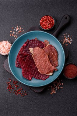 Kurutulmuş et, tuz ve baharatla birlikte koyu beton arka planda dilimler.