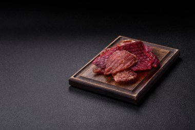 Kurutulmuş et, tuz ve baharatla birlikte koyu beton arka planda dilimler.