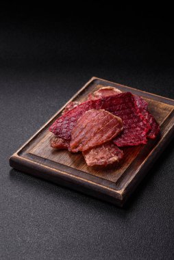 Kurutulmuş et, tuz ve baharatla birlikte koyu beton arka planda dilimler.