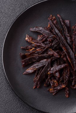 Kurutulmuş at eti ya da koyu beton arka planda tuz ve baharatlı biftek dilimleri.