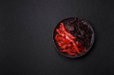 Kurutulmuş, tuzlu ve baharatlı tavuk dilimleri koyu beton arka planda.