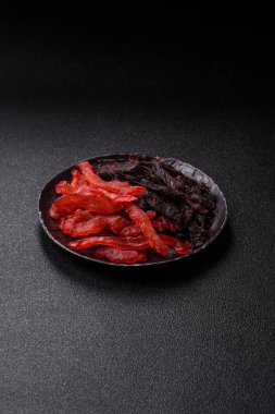 Kurutulmuş, tuzlu ve baharatlı tavuk dilimleri koyu beton arka planda.