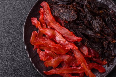 Kurutulmuş, tuzlu ve baharatlı tavuk dilimleri koyu beton arka planda.