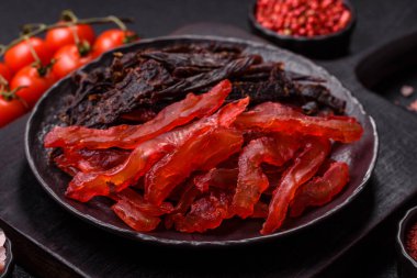 Kurutulmuş, tuzlu ve baharatlı tavuk dilimleri koyu beton arka planda.