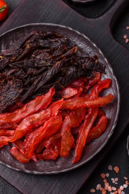 Kurutulmuş, tuzlu ve baharatlı tavuk dilimleri koyu beton arka planda.