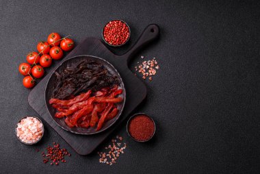 Kurutulmuş, tuzlu ve baharatlı tavuk dilimleri koyu beton arka planda.