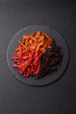 Kurutulmuş, tuzlu ve baharatlı tavuk dilimleri koyu beton arka planda.