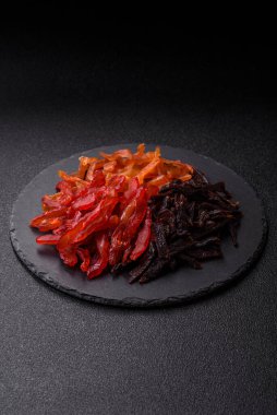 Kurutulmuş, tuzlu ve baharatlı tavuk dilimleri koyu beton arka planda.