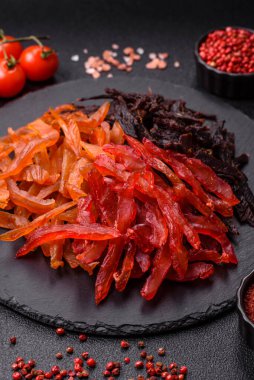 Kurutulmuş, tuzlu ve baharatlı tavuk dilimleri koyu beton arka planda.