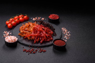 Kurutulmuş, tuzlu ve baharatlı tavuk dilimleri koyu beton arka planda.